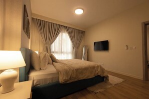 Una camera da letto con un letto, una lampada da comodino, un televisore montato a parete e una finestra con tende.