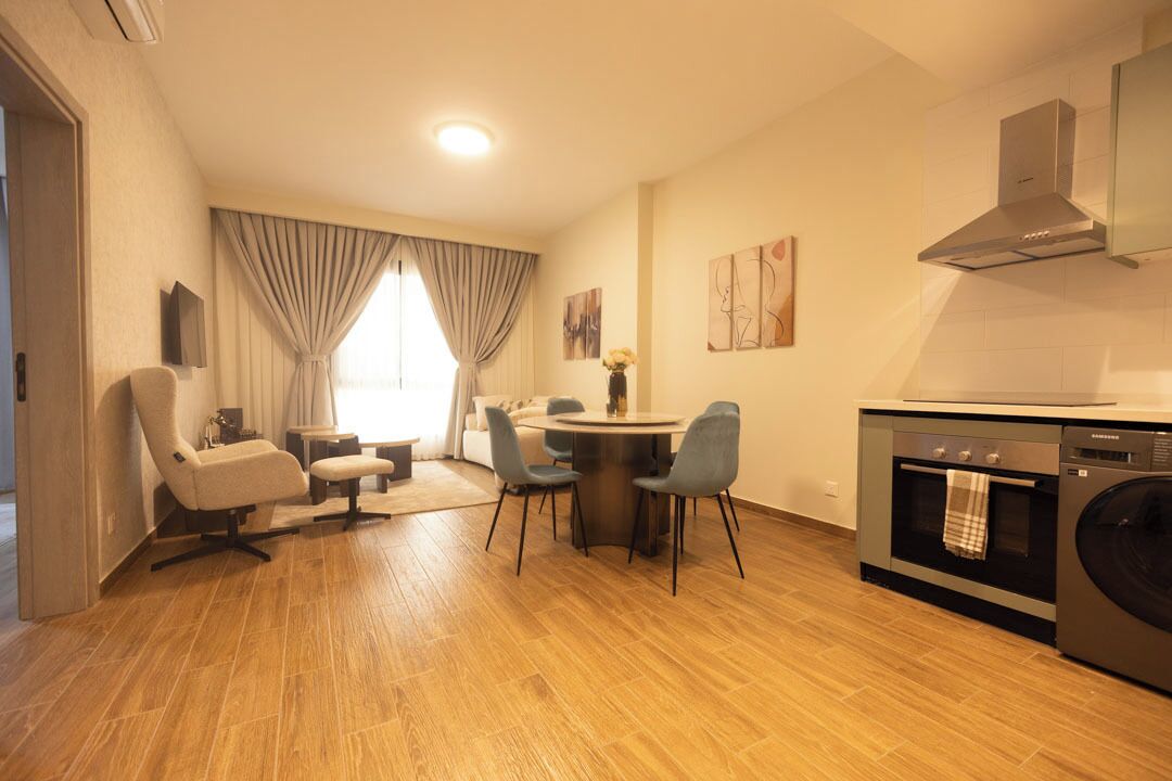 A modern living room with a dining area, a sofa, a coffee table, and a kitchen with a washing machine.