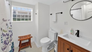 A bathroom with a toilet, sink, mirror, and window.