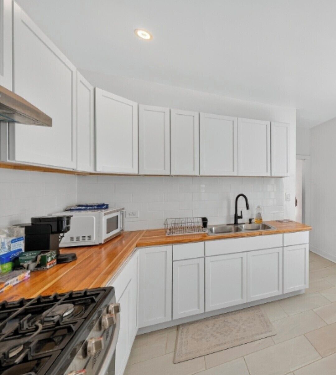 Une cuisine moderne avec des meubles blancs, un four à micro-ondes, une cuisinière et un plan de travail en bois.