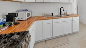 A modern kitchen with white cabinets, a microwave, a stove, and a wooden countertop.