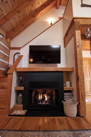 Ein Zimmer mit Kamin, einem darüber montierten Fernseher und Holzbalken an der Decke.