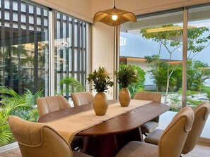 A modern dining area with a round table, six chairs, two vases with plants, and large windows offering a view of greenery and a building. - 1 mile to the BEACH-amazing 3 bedroom condo W/AC in Playa del Carmen at The LEAF (Playa del Carmen)