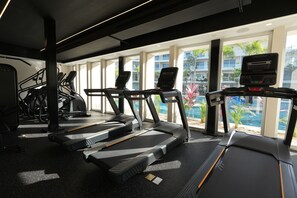 Ein Fitnessstudio mit Laufbändern, Ergometer und einem großen Fenster mit Blick auf Gebäude und Grünflächen.