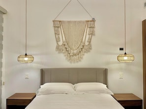 Ein Schlafzimmer mit einem Bett, zwei Nachttischen, einem Wandbehang aus Makramee und zwei Pendelleuchten.