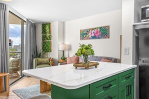 Eine moderne Küche mit Marmorarbeitsplatte, grünen Schränken und einem Essbereich mit einer Couch und einem Tisch.