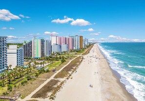 Eine Küstenlandschaft mit hoch aufragenden Gebäuden, einem Sandstrand und einem strahlend blauen Himmel.