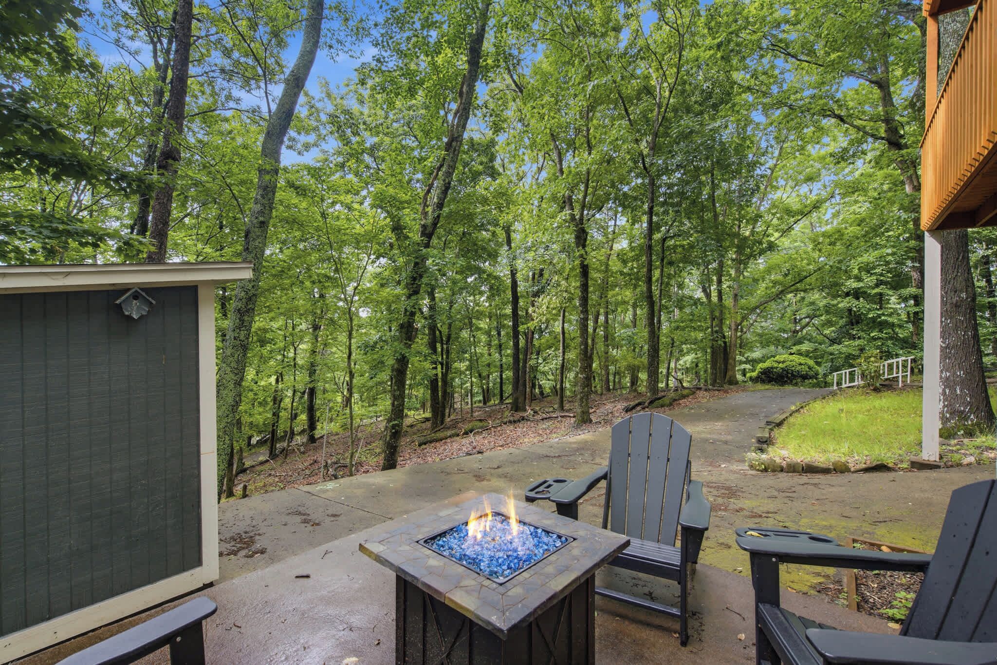 An outdoor patio with a fire pit, seating, and a view of a wooded area.