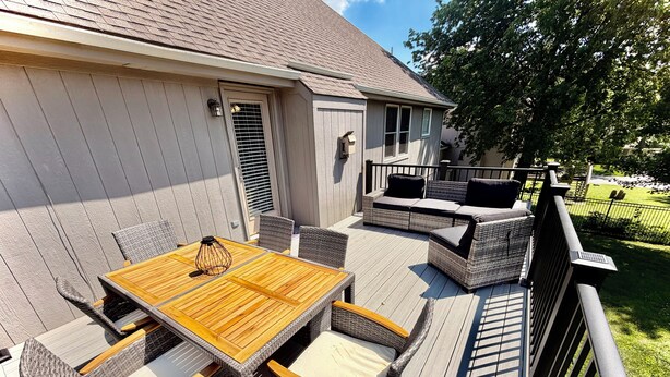 A deck with a wooden table and wicker chairs, a covered seating area, and a view of a house.