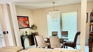 A living room with a sofa, a dining table with chairs, a chandelier, and a painting on the wall.