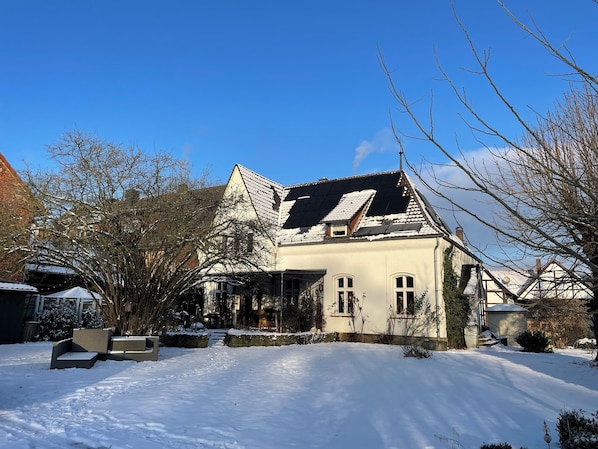 Ein Haus mit geneigtem Dach, einer Veranda und einem schneebedeckten Vorgarten.