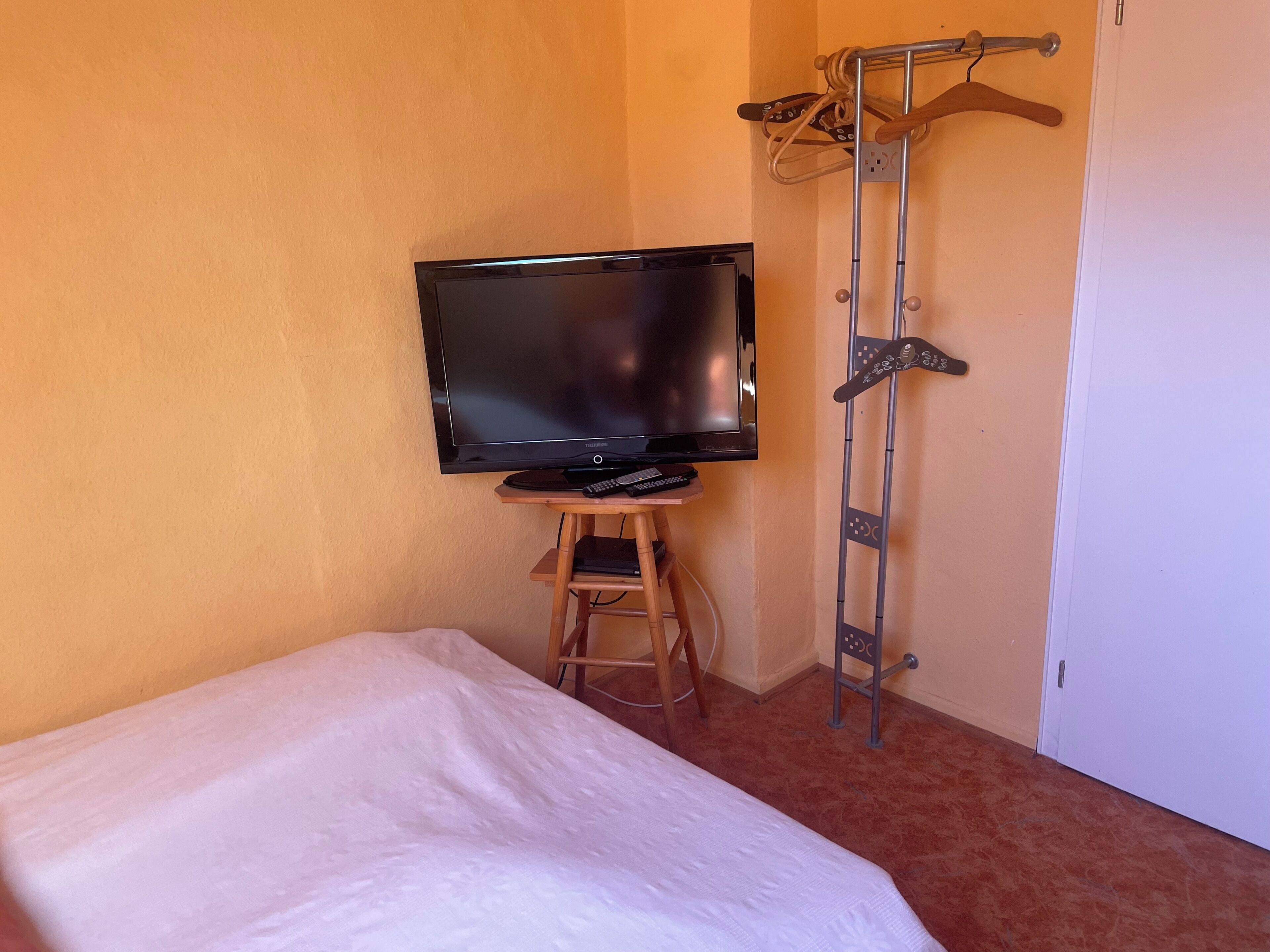 A room with a bed, a television on a wooden stand, a metal coat rack, and a door.