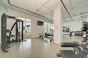 Ein Fitnessraum mit Trainingsgeräten, großen Fenstern und Blick auf den Strand.