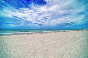 Ein Strand mit klarem Wasser, einem weiten Sandstrand und einem teils bewölkten Himmel.