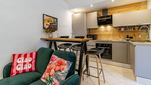 A modern kitchen with a wooden countertop, a dining area with a table and chairs, and a green sofa with floral cushions.