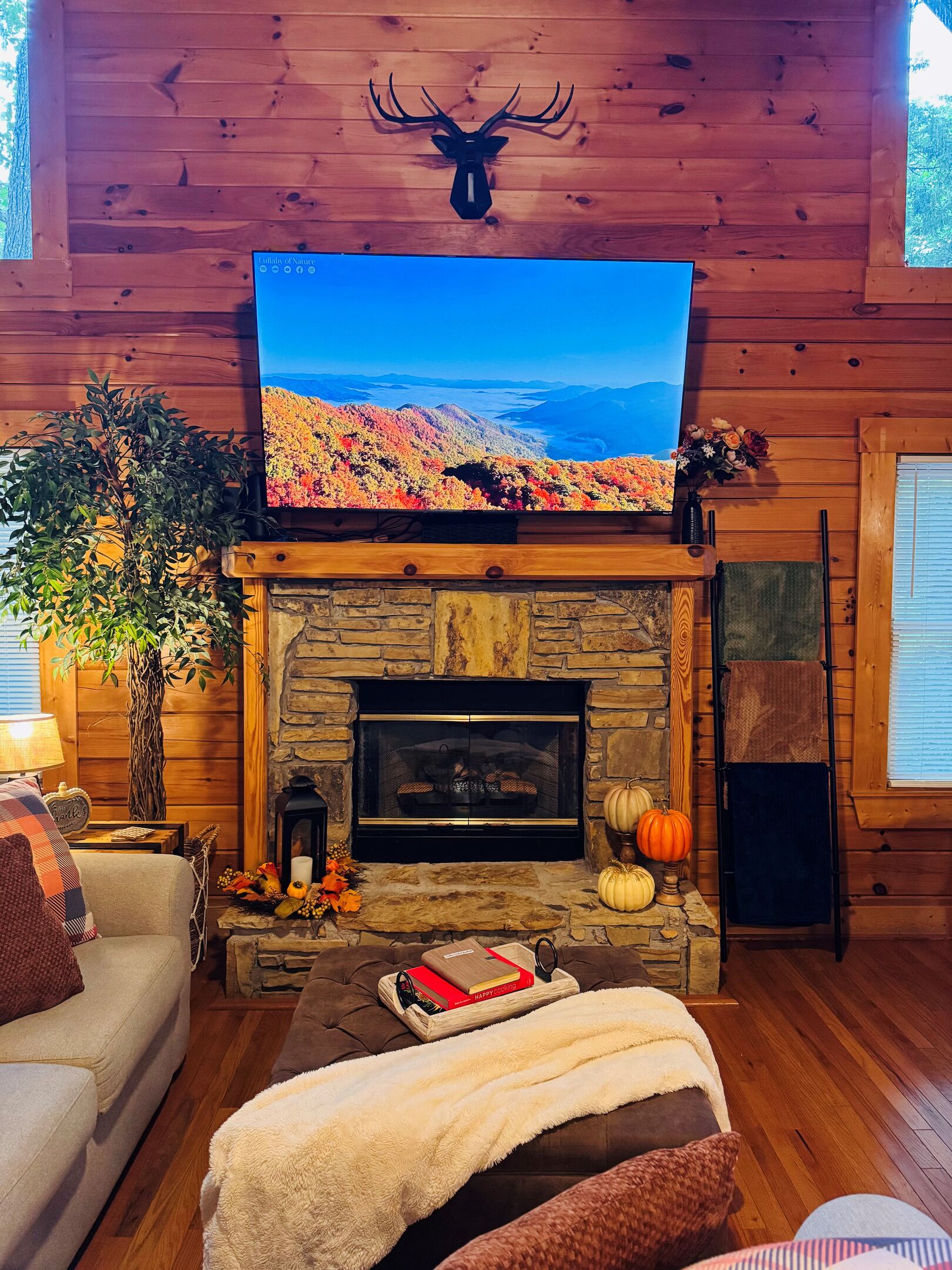 A cozy living room with a stone fireplace, a television mounted above it, and a deer head decoration on the wall.