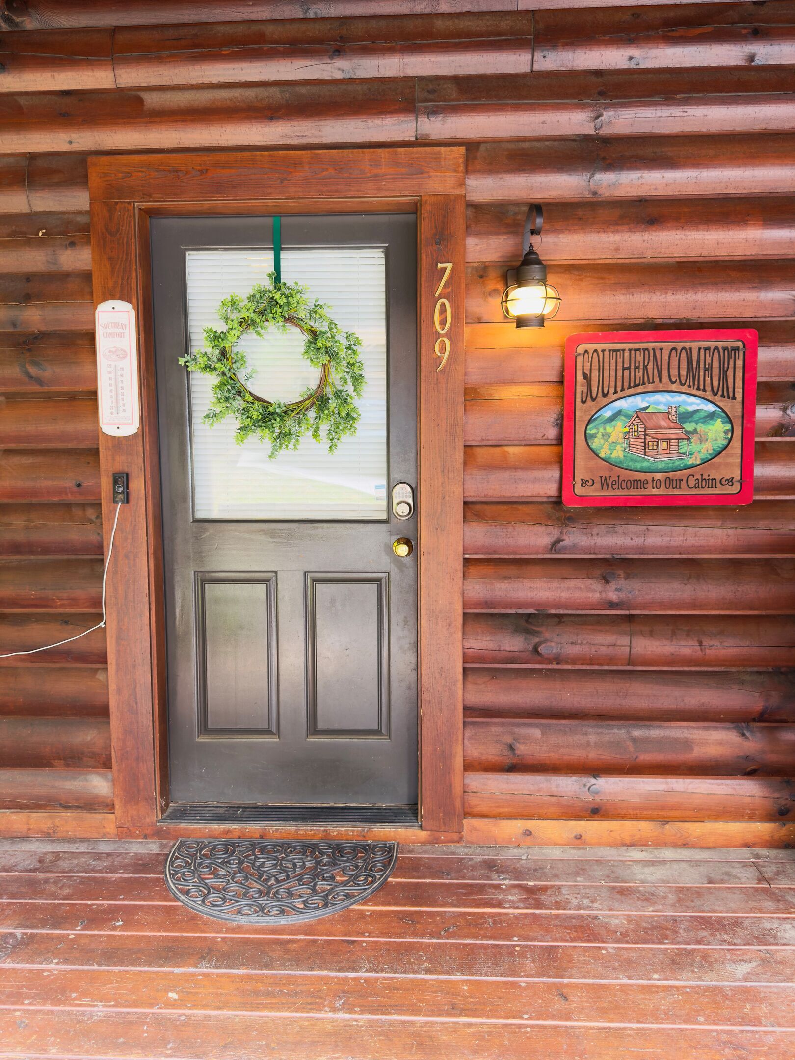 A wooden cabin door with a green wreath, a number '709' above it, and a 'Southern Comfort' sign on the right.
