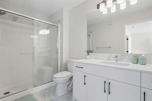 Un bagno moderno con box doccia in vetro, un WC e mobili bianchi.