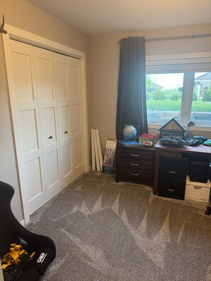 A room with a large white closet, a desk with various items, a globe, and a window with a view of greenery.