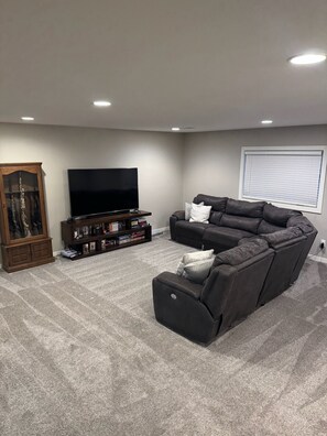 A living room with a sectional sofa, a flat-screen TV, a bookshelf, and a cabinet.