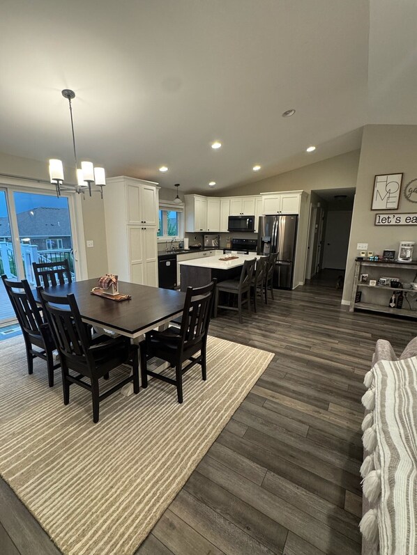 A modern kitchen with white cabinets, a central island, and a dining area with a dark wooden table and chairs.