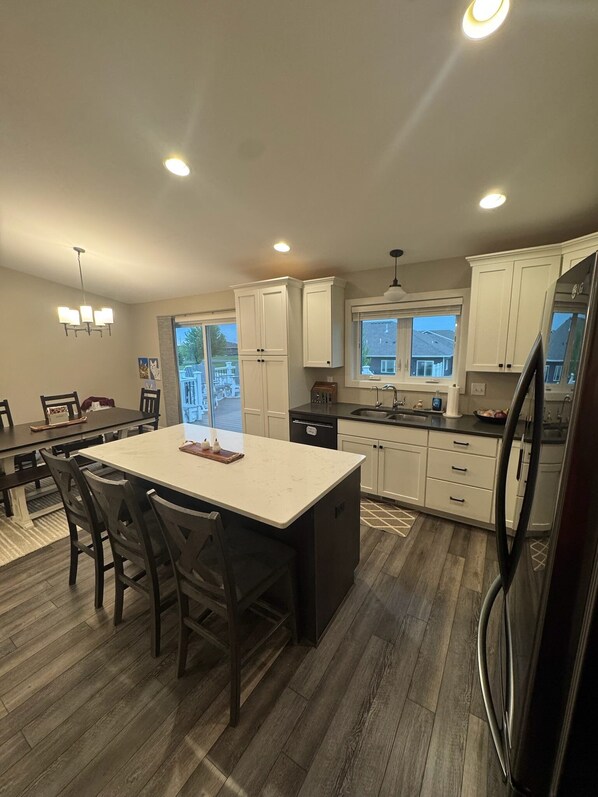 A modern kitchen with white cabinets, a central island, and a dining area with wooden chairs.