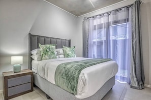 Ein Schlafzimmer mit Bett, Nachttisch, Lampe und durchsichtigen Vorhängen.