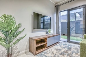 Ein modernes Wohnzimmer mit einem großen Flachbildfernseher, einer Holzkonsole und einer Schiebeglastür, die auf eine Terrasse führt.