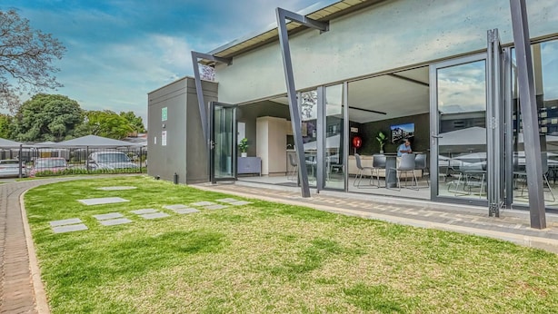 Un bâtiment moderne doté d’une façade en verre, d’un espace extérieur aménagé pour s’asseoir et d’un chemin piétonnier pavé.