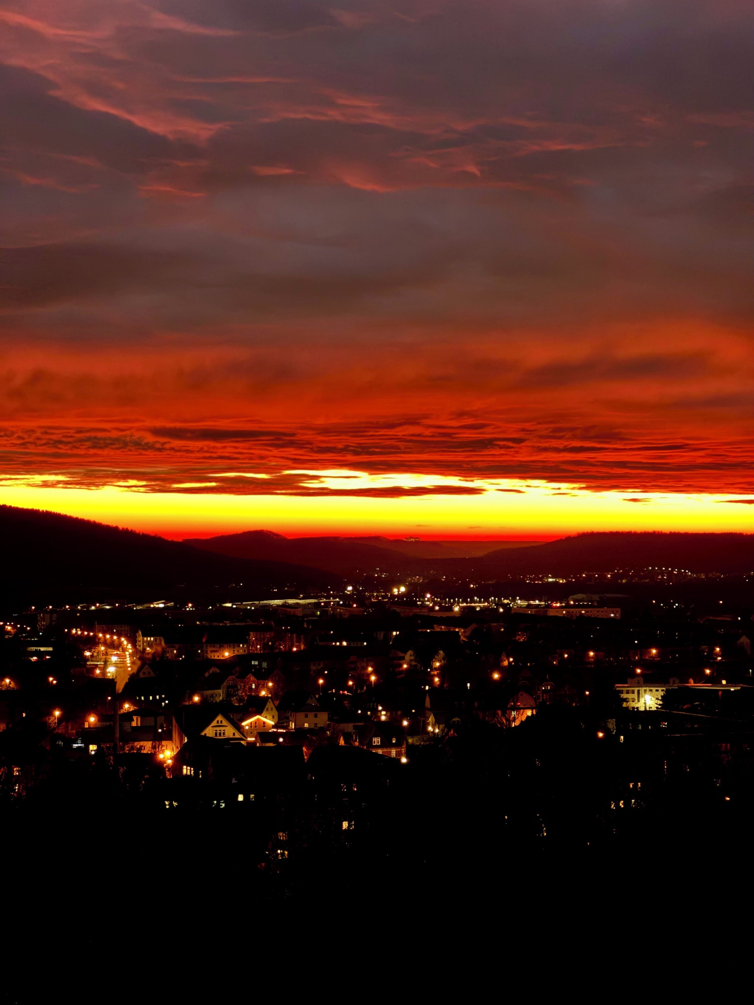 A cityscape at dusk with a sunset over a range of hills.