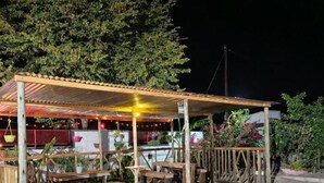 Un espacio al aire libre techado con bancos y mesas de madera, rodeado por una valla de madera y plantas.