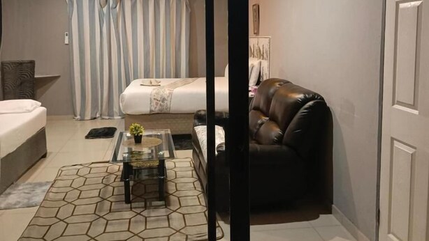 Una sala moderna con sofá, una mesa de centro, un tapete estampado, una cama con cortinas a rayas y una puerta.