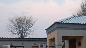 Un edificio con techo gris, varias unidades de aire acondicionado y un patio empedrado con plantas en macetas.