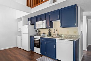 A modern kitchen with white appliances, blue cabinets, and a granite countertop. - Eagle's View Condo at Fall Creek (Branson)