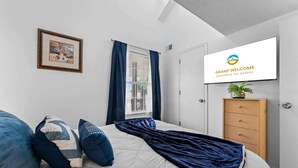 A bedroom with a bed, pillows, a window with curtains, a TV on the wall, and a wooden cabinet. - Eagle's View Condo at Fall Creek (Branson)