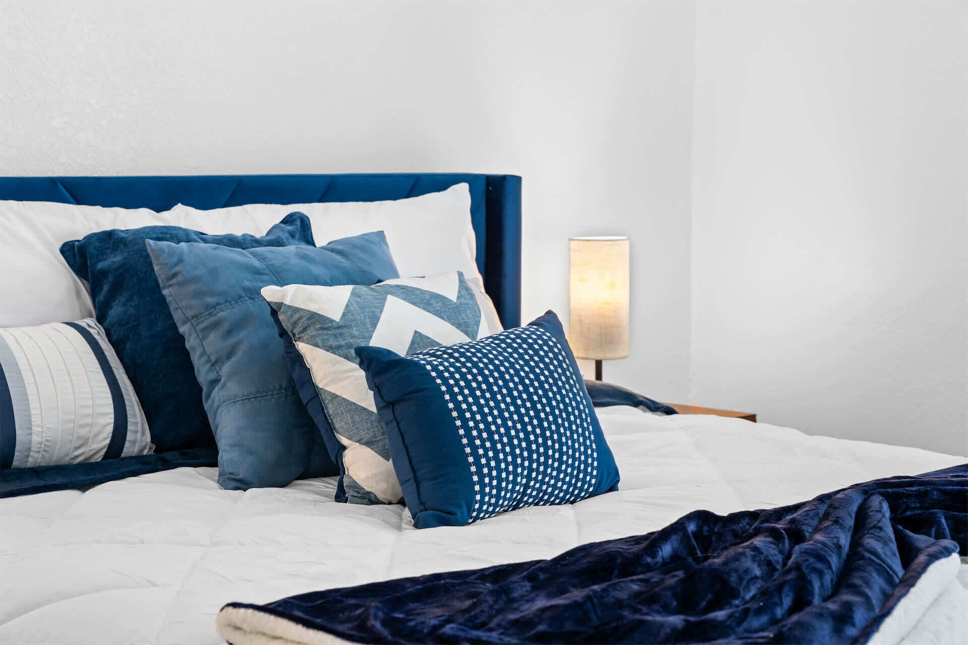 A bed with a white duvet, blue pillows, and a dark blue blanket.