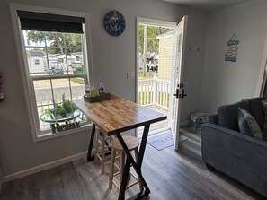 A compact kitchen with a wooden table, bar stools, a gray couch, and a view of the outside.