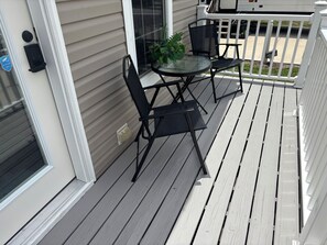 A deck with a glass-top table and two chairs, a potted plant, and a white railing.