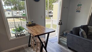 Een keuken met een houten tafel en krukken, een grijze bank en een uitzicht op een woonwijk door een raam.