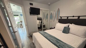 Een slaapkamer met een bed, een televisie en een deur naar een andere kamer.