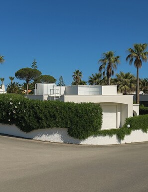 Un bâtiment moderne à la façade blanche, doté d’un garage et d’une haie bien entretenue.