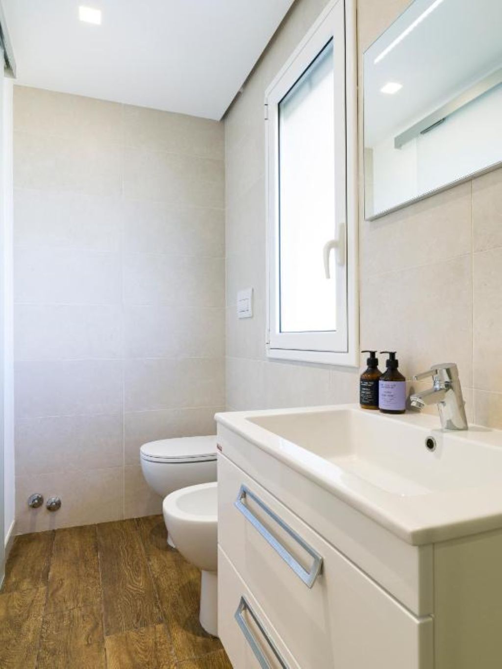 Ein Badezimmer mit Toilette, Waschbecken mit Spiegel und zwei Seifenflaschen.