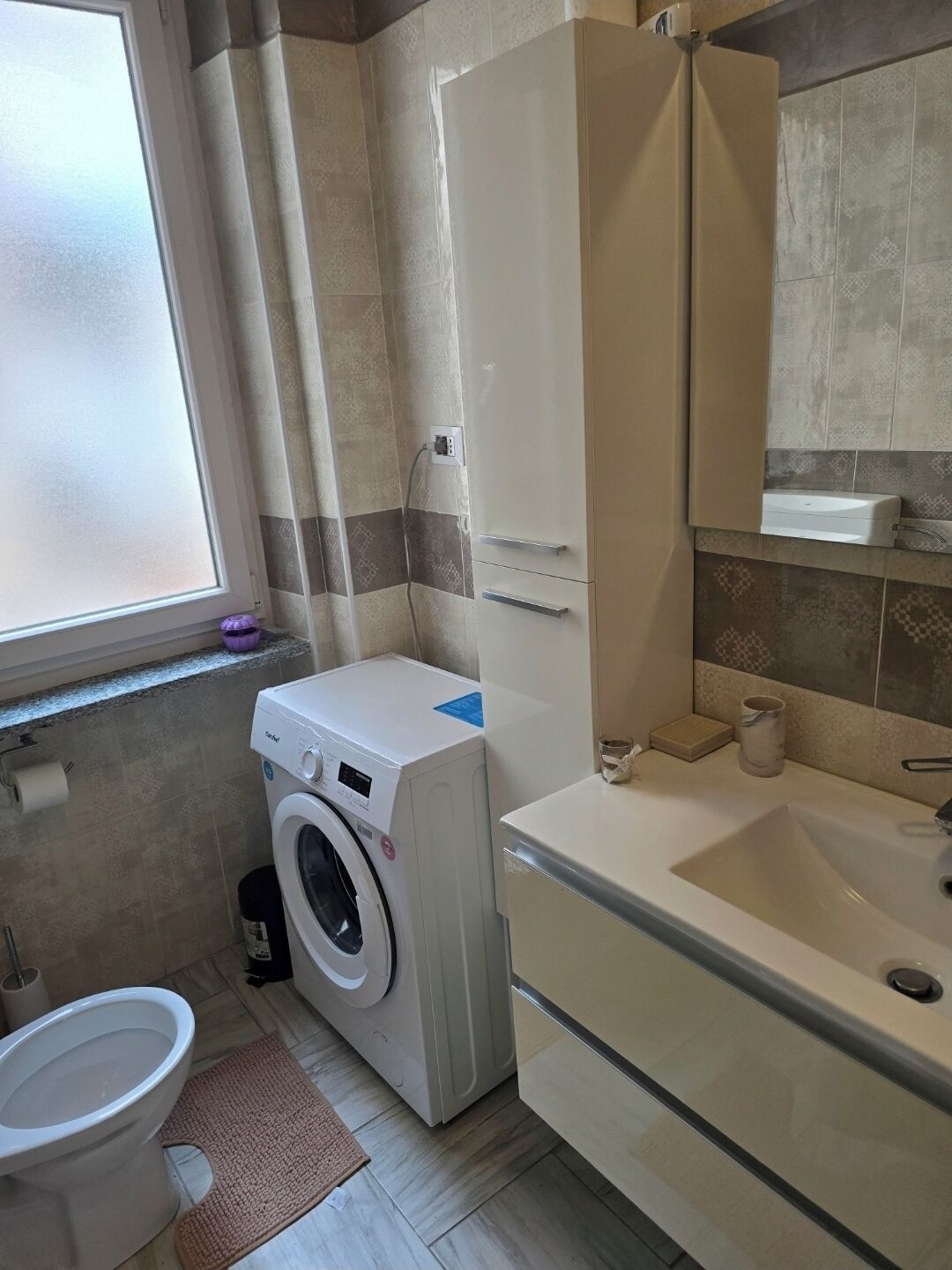 A compact bathroom with a washing machine, toilet, and sink.