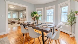Un espace repas avec une longue table, des chaises blanches et une plante en pot.