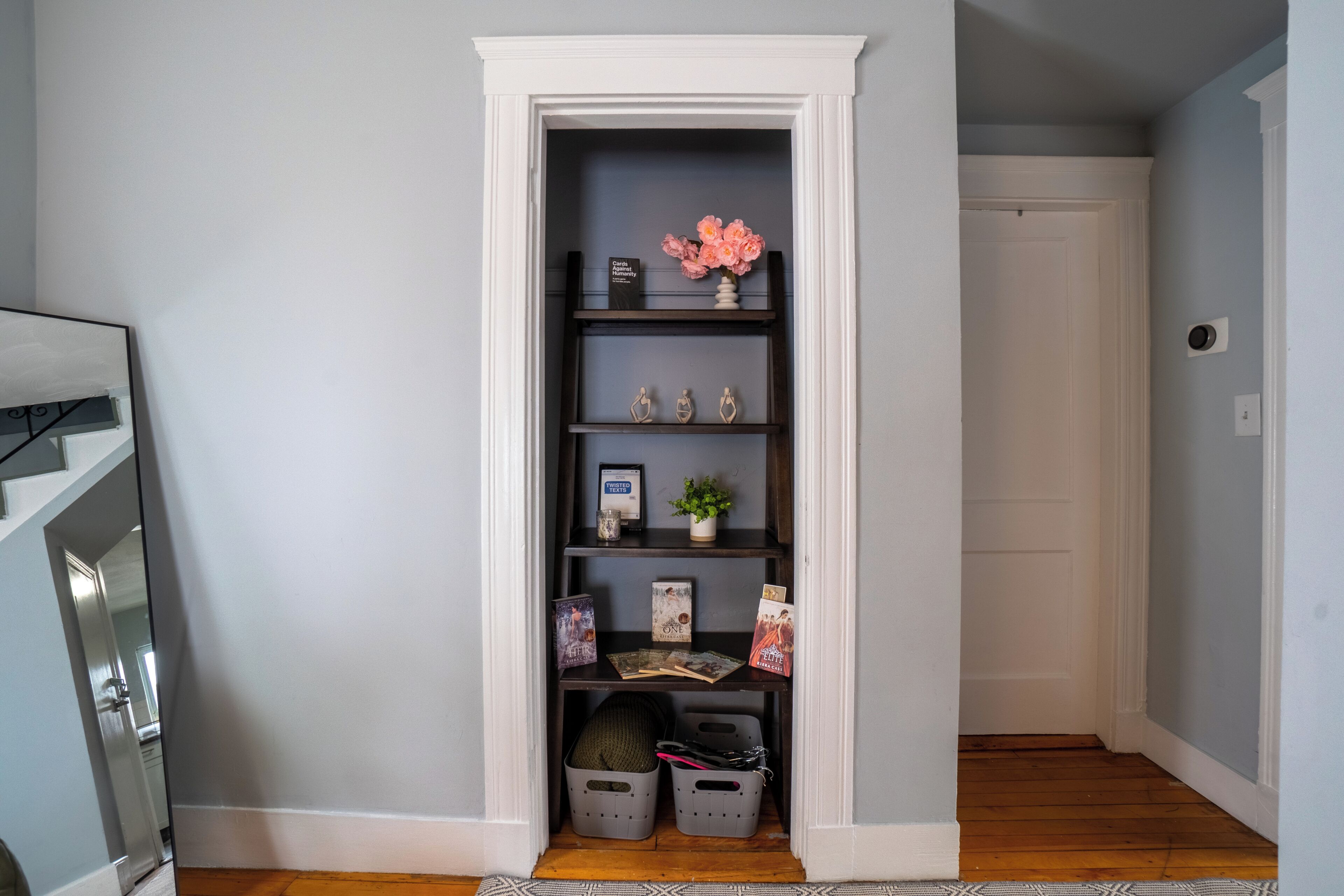 A narrow hallway with a built-in shelving unit containing books, decorative items, and storage bins.