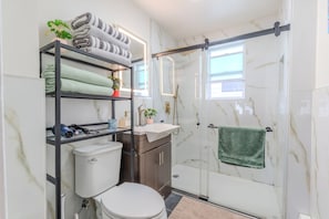 Ein Badezimmer mit Toilette, Waschbecken, Dusche und Regalen mit Handtüchern.