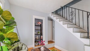 Un escalier avec une rampe en métal, une table basse en bois sur laquelle se trouvent un livre et une plante, un fauteuil vert et une bibliothèque agrémentée d’objets décoratifs.