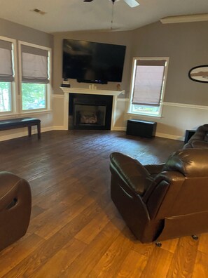 Een woonkamer met een open haard, een televisie erboven en een bruine leren bank.