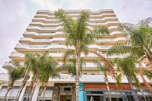 Un hôtel à plusieurs étages doté de balcons, de palmiers et de boutiques, notamment un snack et un restaurant-grill.