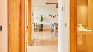 Um corredor com portas de madeira, uma área de jantar com uma planta e um banheiro com pia.
